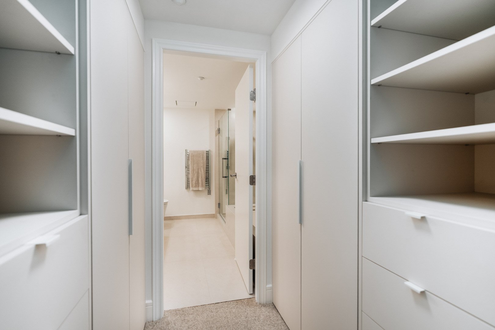 55-00-Symmetrical view down a minimalist custom white walk-in closet leading into a modern Vancouver bathroom.