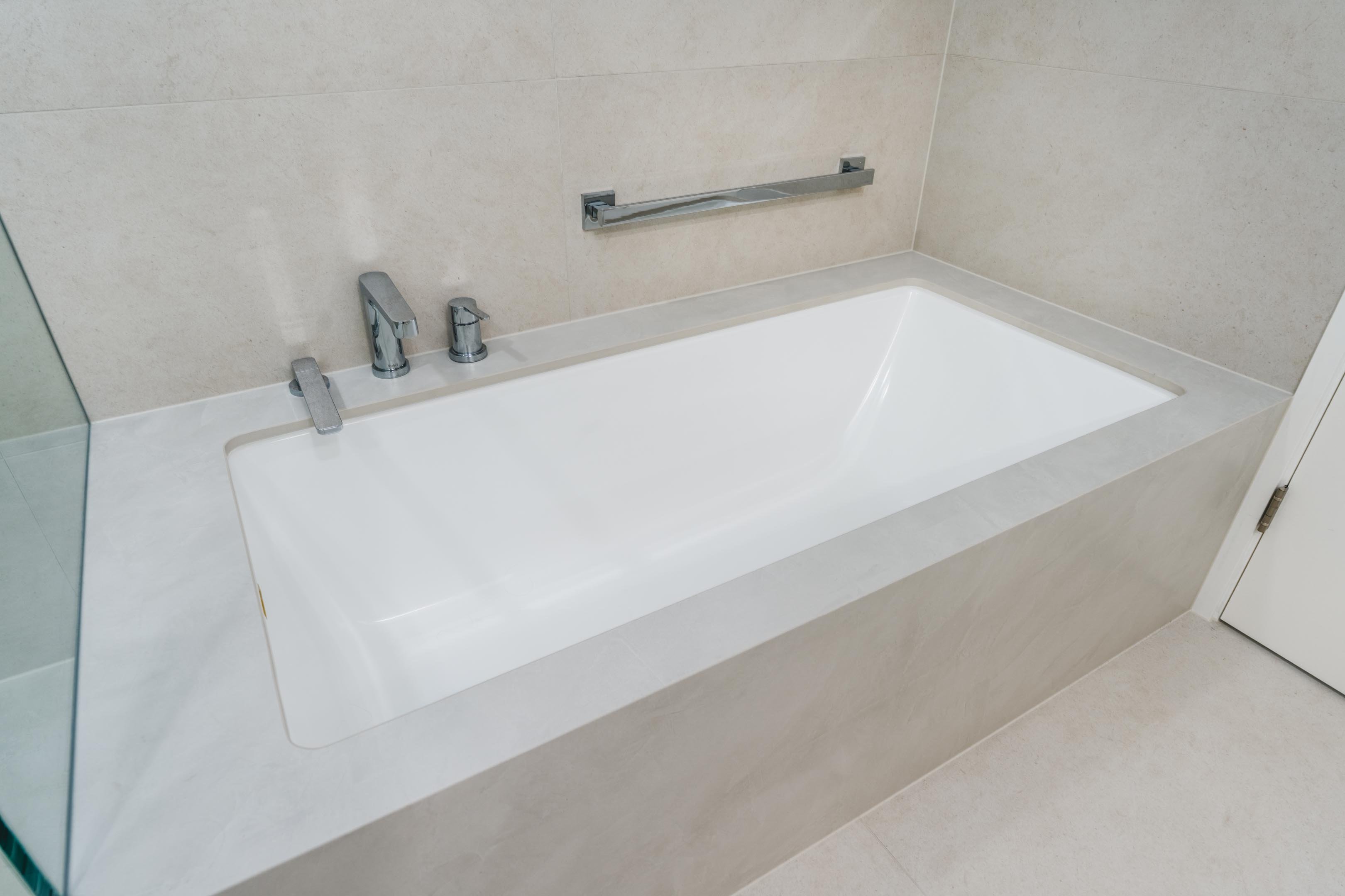 55-00-Minimalist white soaking bathtub with chrome fixtures and gray tile surround in a modern Vancouver home.