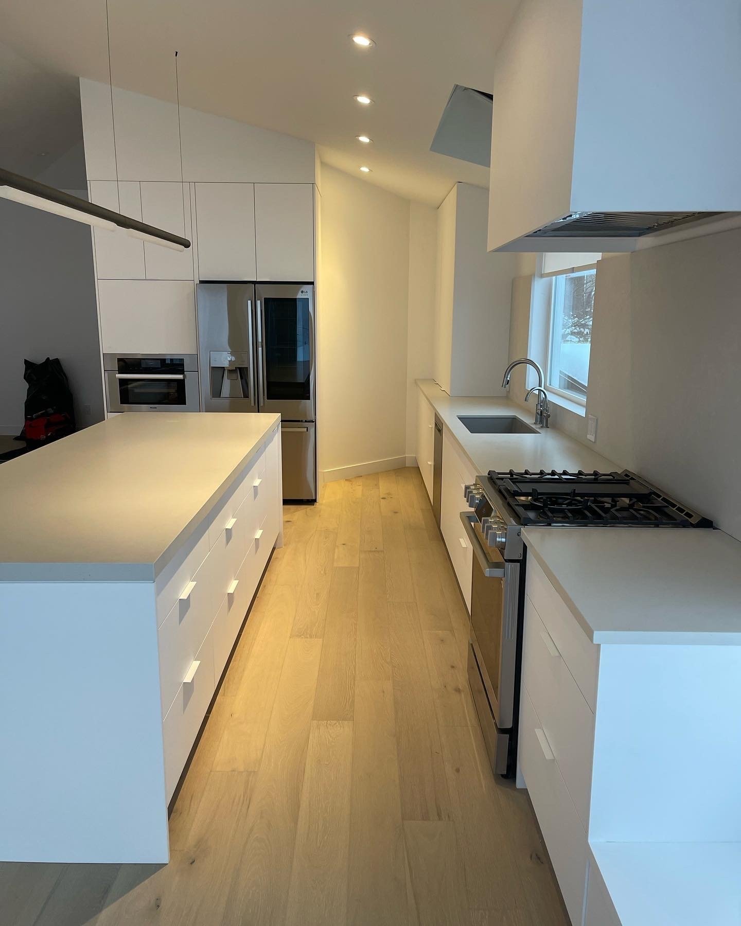 Springer Ave-Modern white galley kitchen in Vancouver with hardwood floors, integrated appliances, and long island