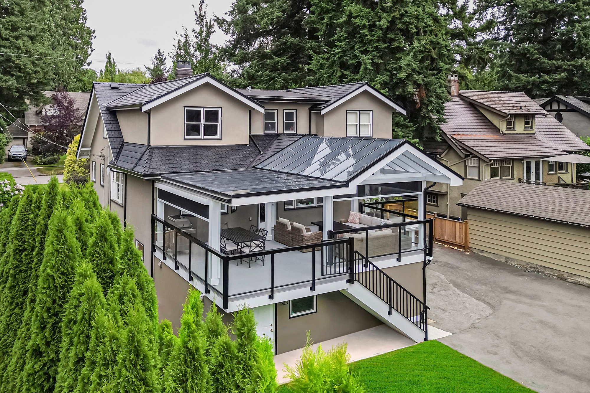 Aerial view of a house with a large covered deck featuring glass roofing, dark railings, outdoor seating, and a dining area.