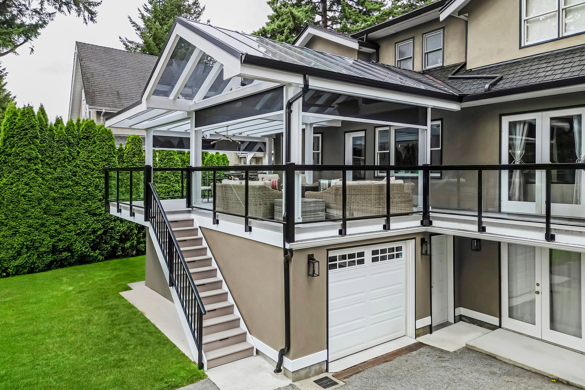 View from the yard showing a house with a raised covered deck, white stairs leading up, and a lower level garage door.