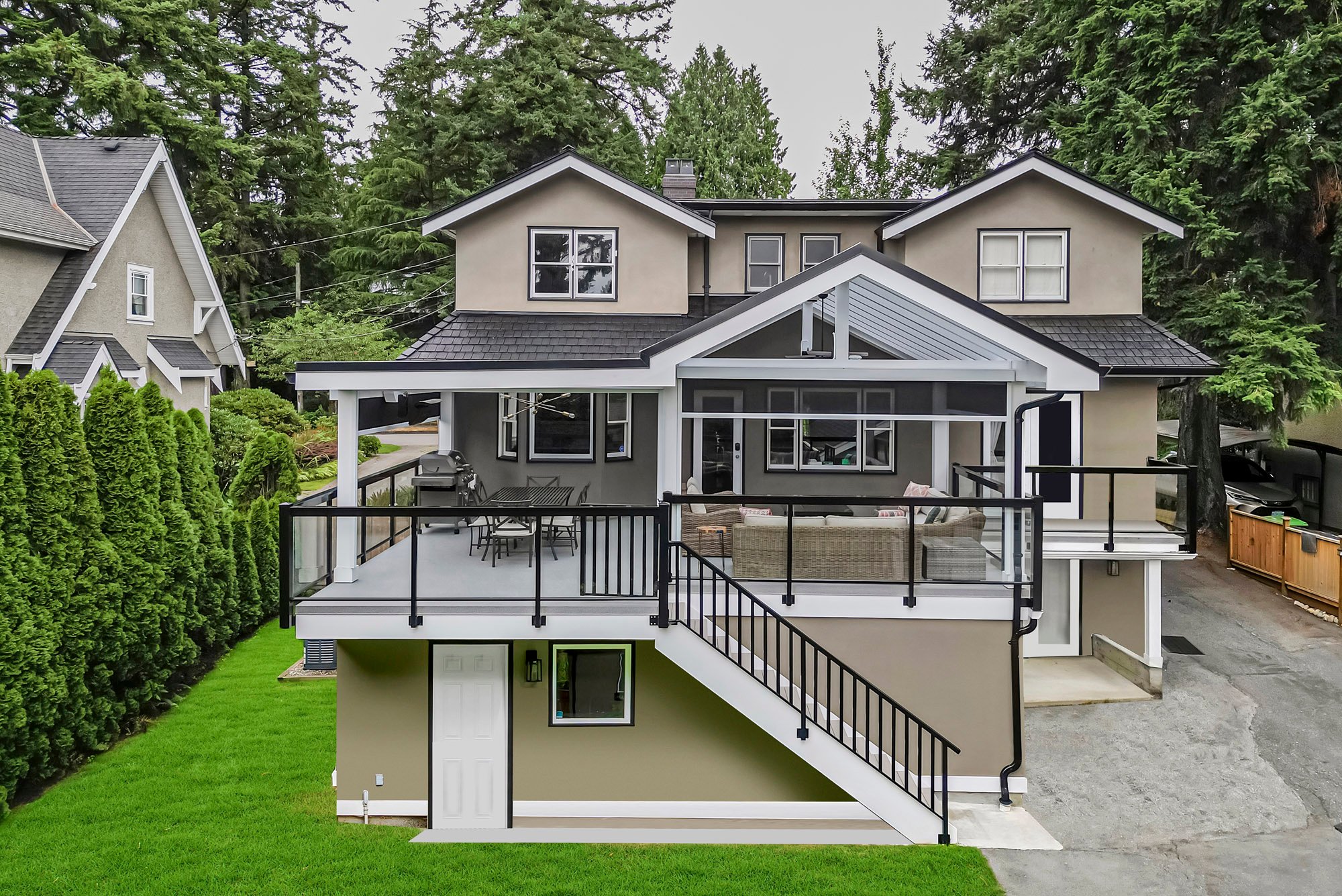 Exterior back view of a grey house with a large elevated covered deck featuring glass railings and white stairs.