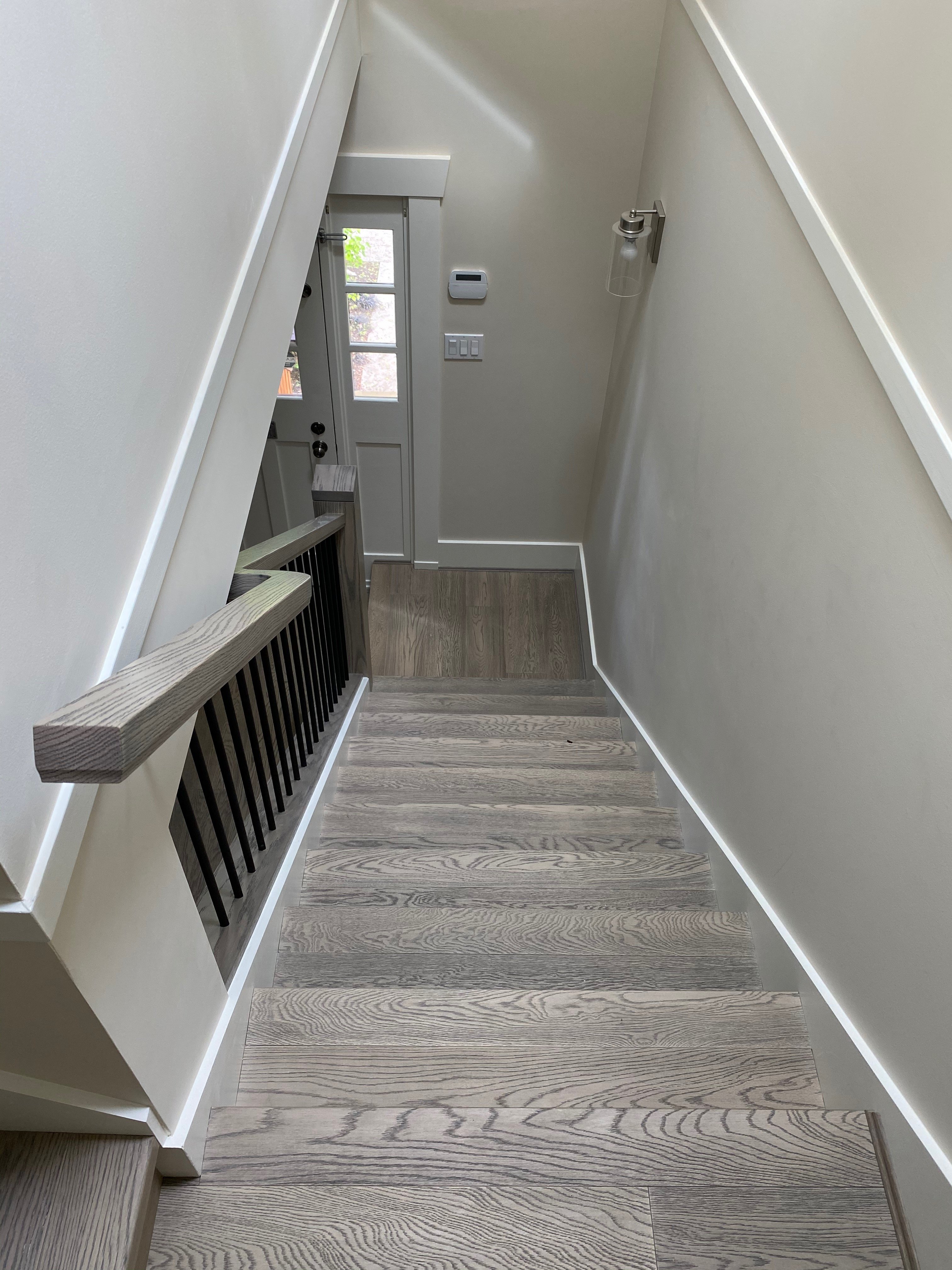 High-angle view descending a grey wooden staircase towards a lower landing featuring an exterior door with glass panes.