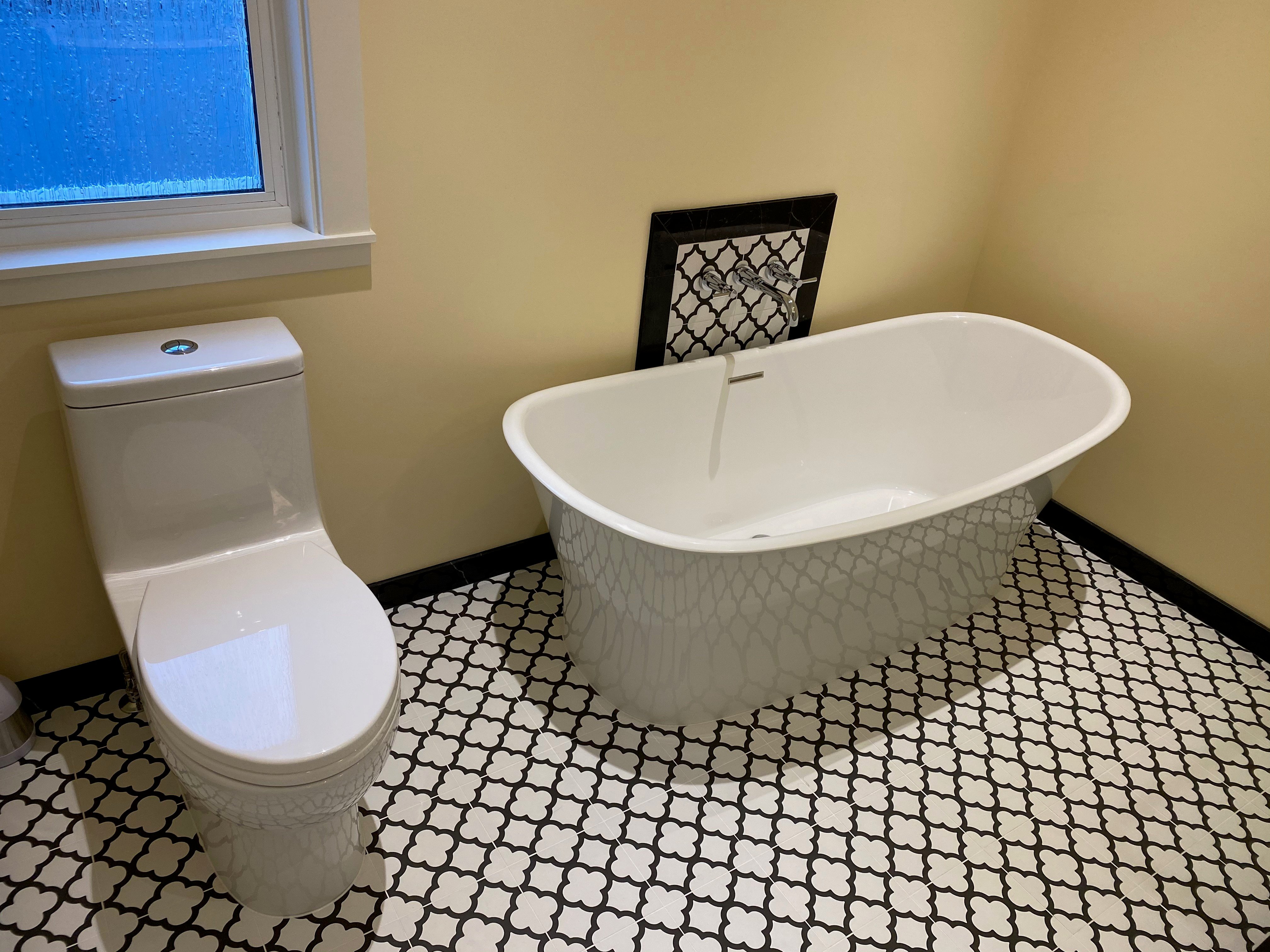 A bathroom with warm yellow walls, a white toilet, a modern freestanding bathtub, and striking black and white floor tiles.