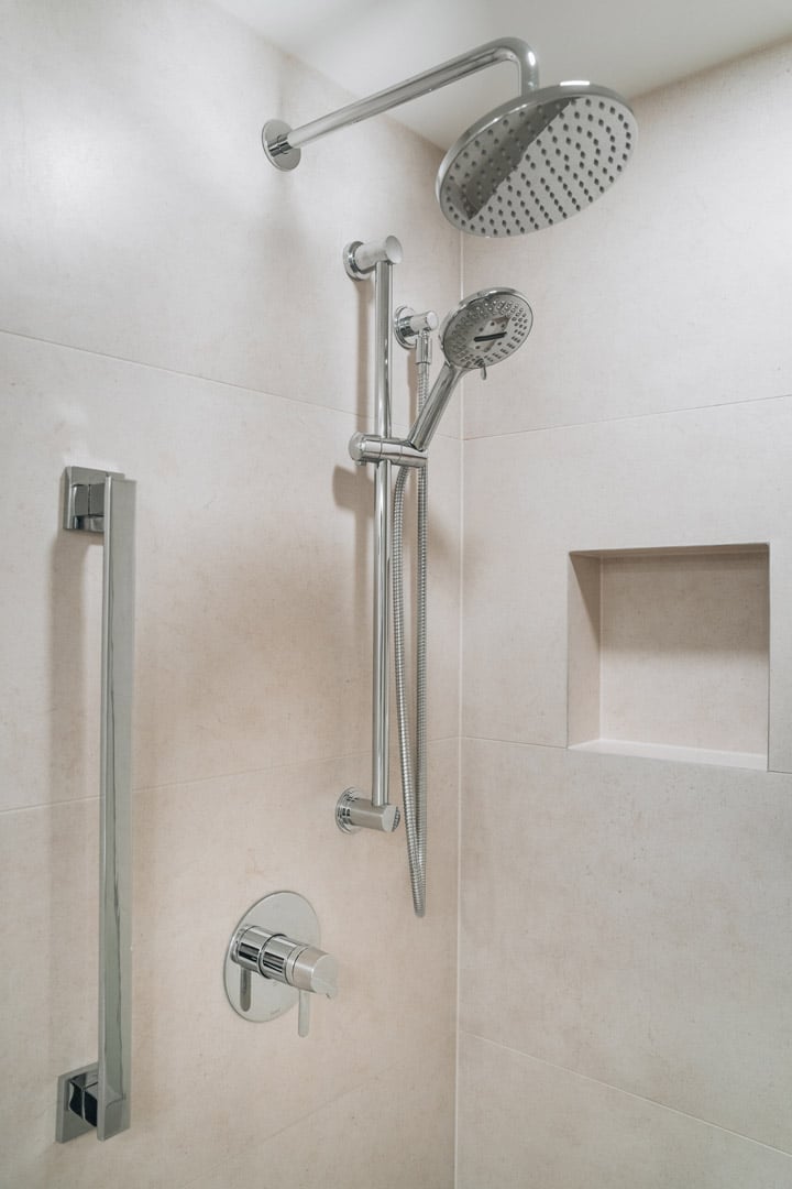 Detail shot of a modern shower featuring beige tiled walls, chrome fixtures including a rain showerhead, and a grab bar.