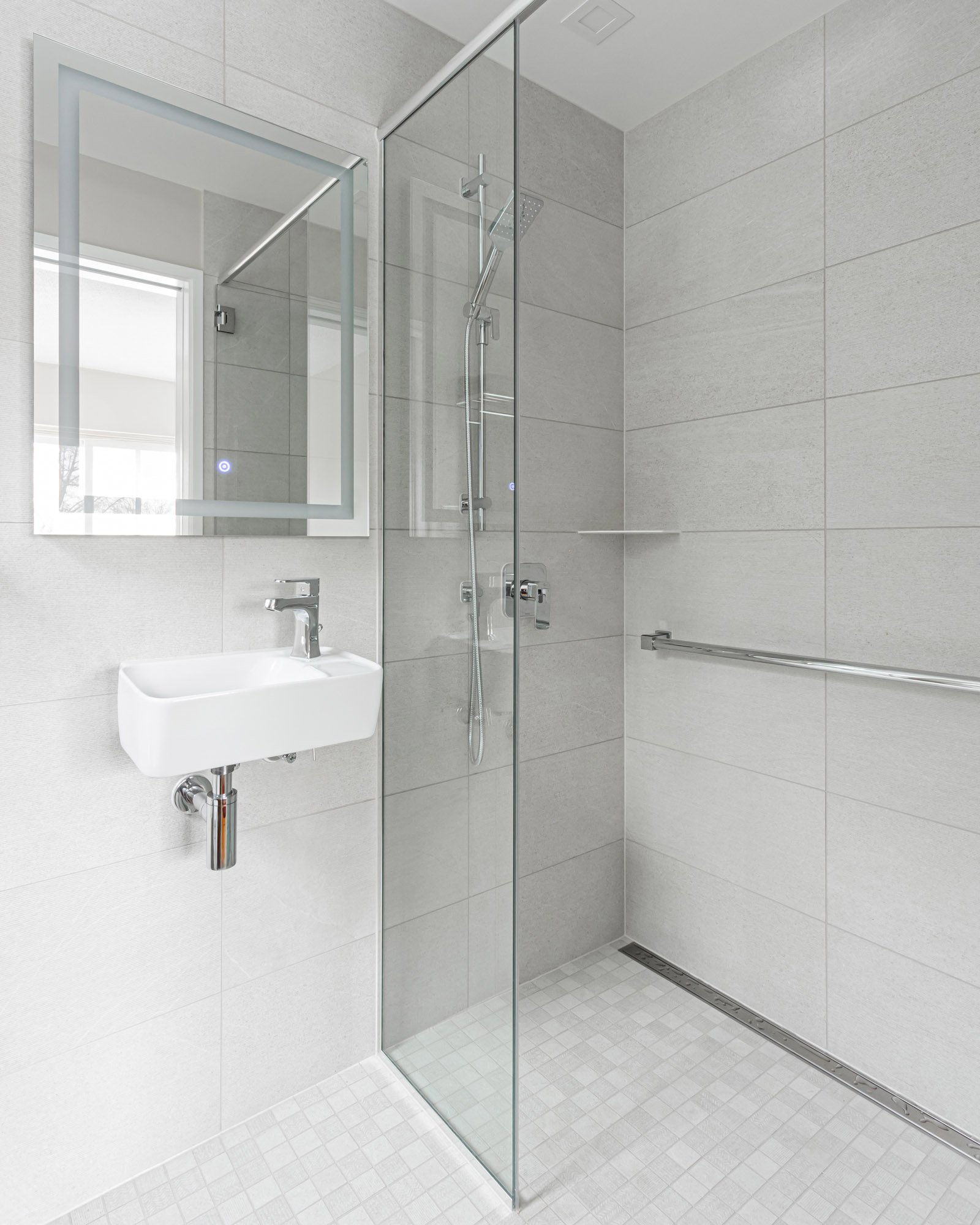 A bright clean bathroom featuring a small wall-mounted sink alongside a glass-enclosed shower stall with chrome fixtures.