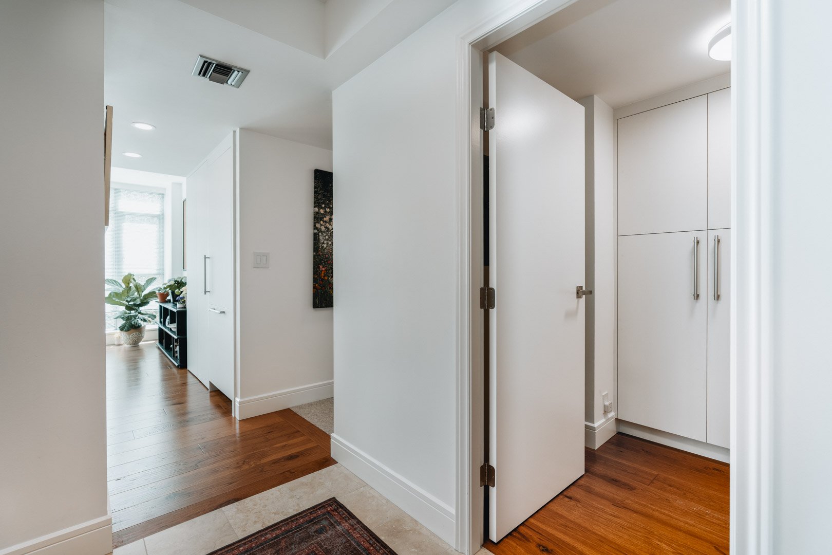 A bright hallway with warm hardwood floors, white walls, and closed white doors leading to different rooms in the house.