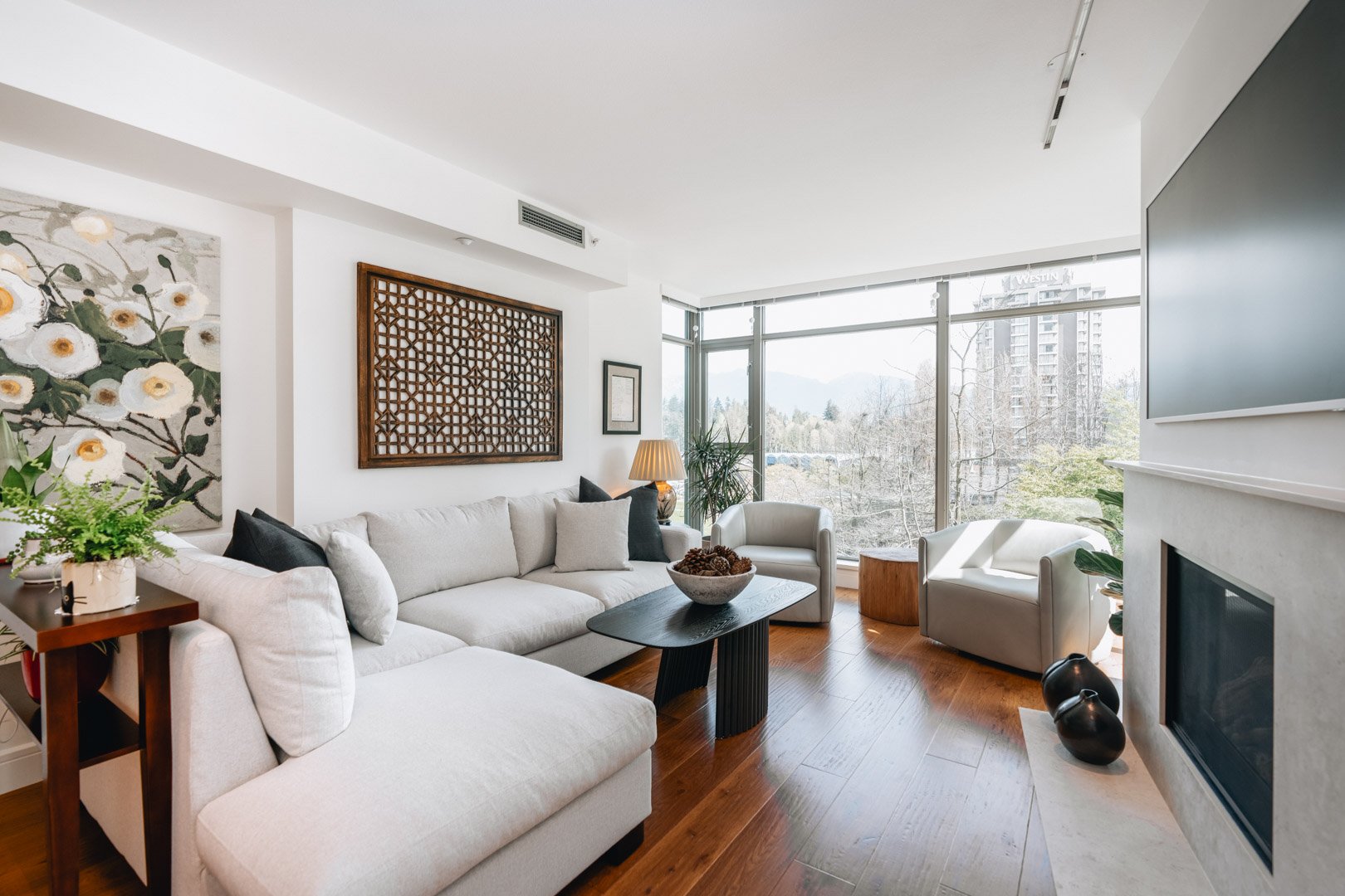 A bright living room featuring a large white sectional sofa, a black coffee table, hardwood floors, and a stone fireplace.