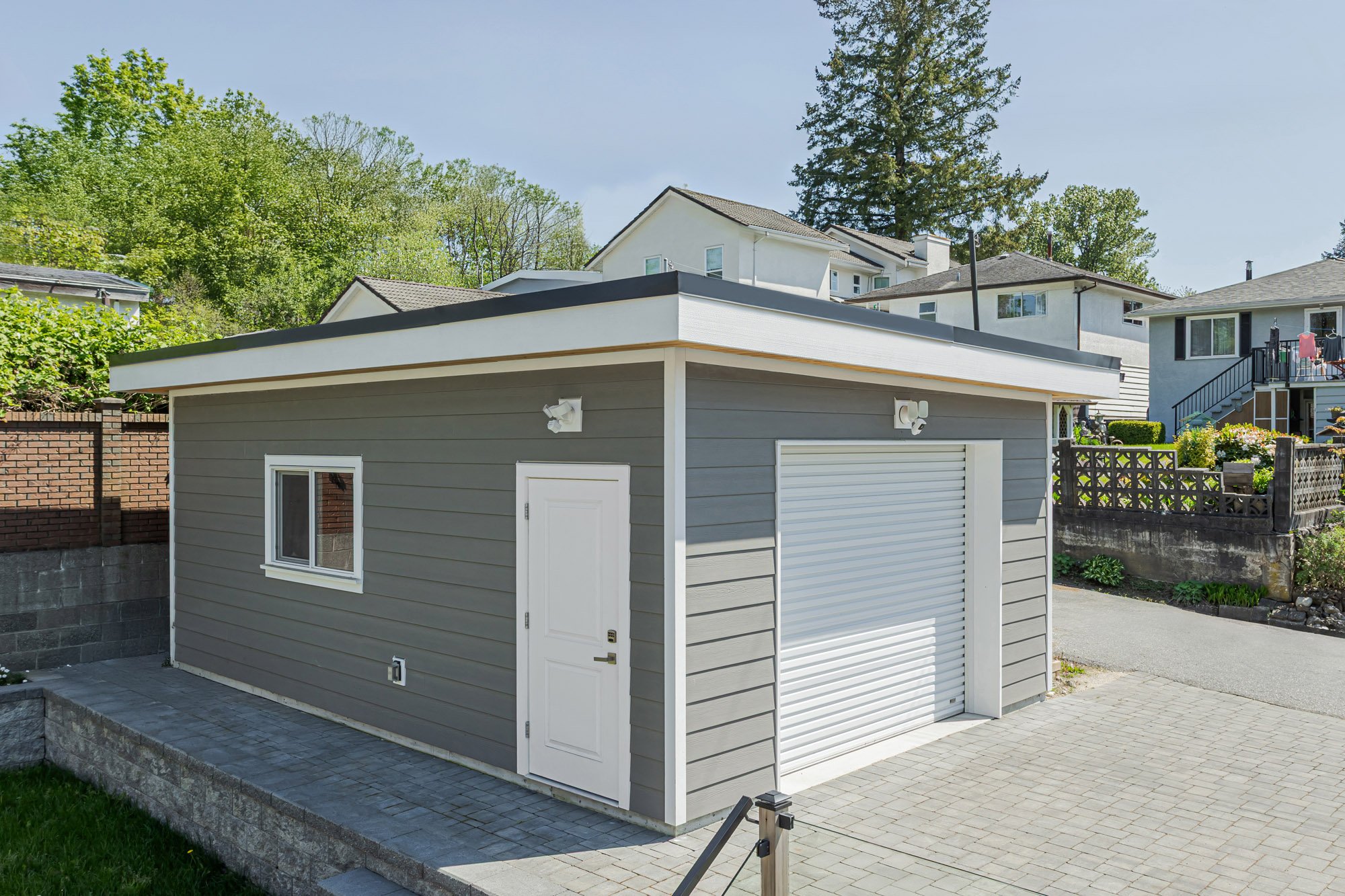 Elevated angled view of a modern grey detached garage featuring a white roll-up door, white side door, and stone driveway.