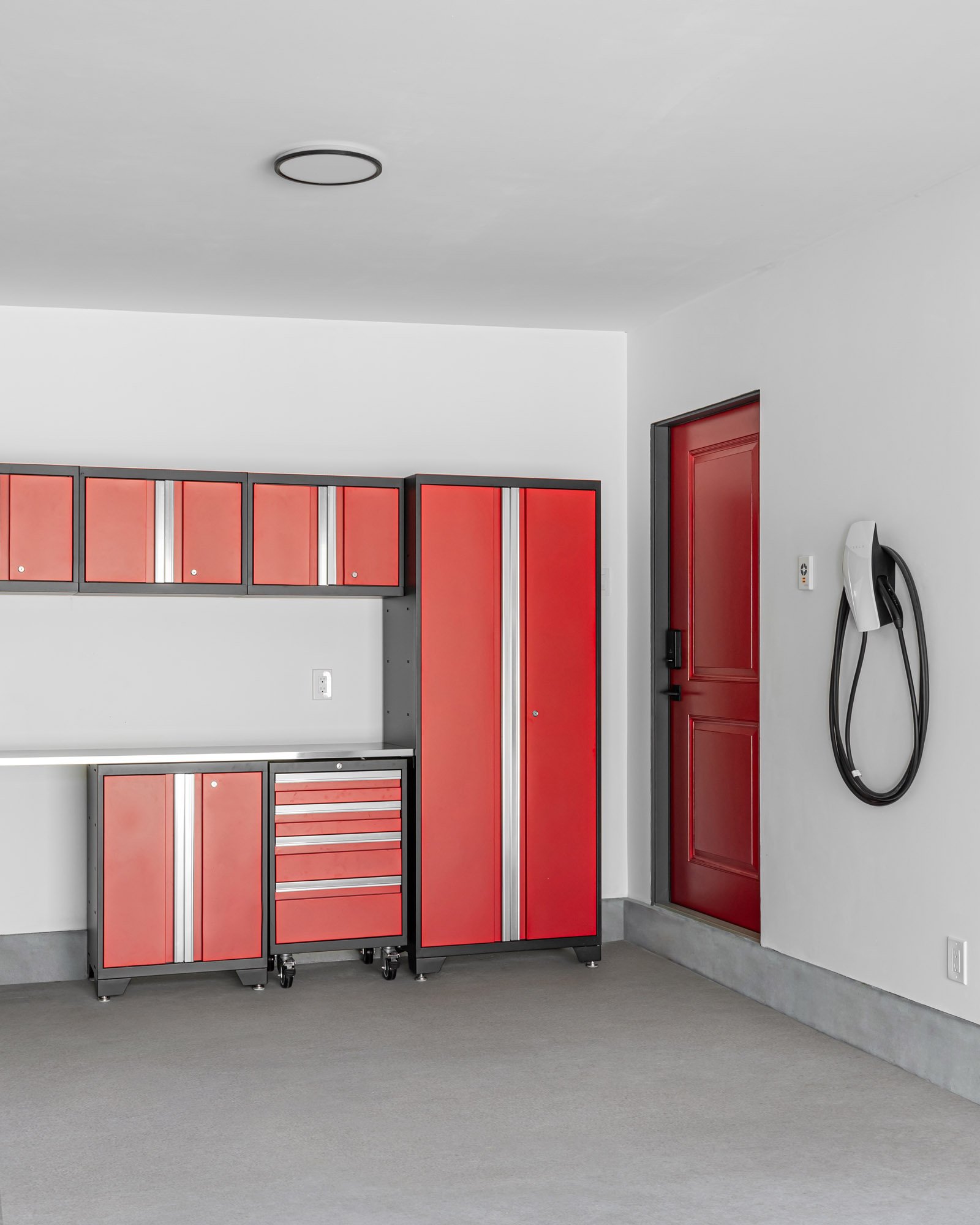 Clean garage interior featuring a bright red metal storage cabinet system, a stainless steel workbench, and an EV charger.