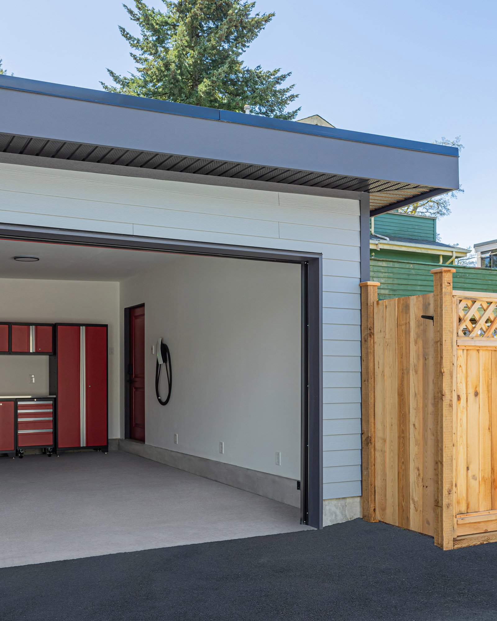 Exterior view of an open grey garage revealing red metal storage cabinets, a smooth floor, and an EV charger mounted inside.
