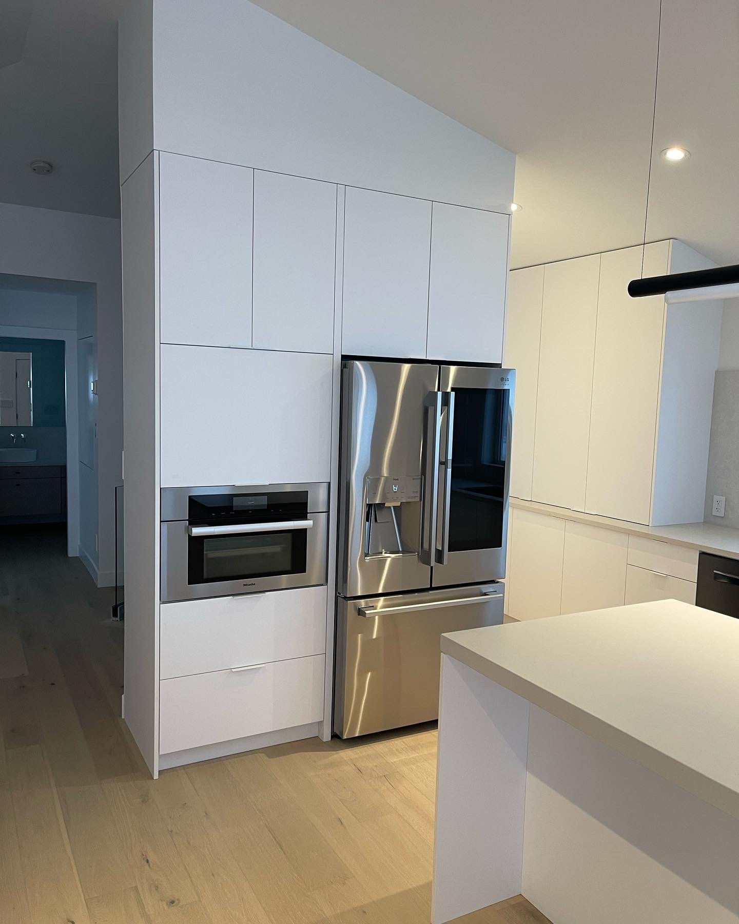 Built-in white kitchen cabinets housing a modern stainless steel wall oven and microwave unit next to a large refrigerator.