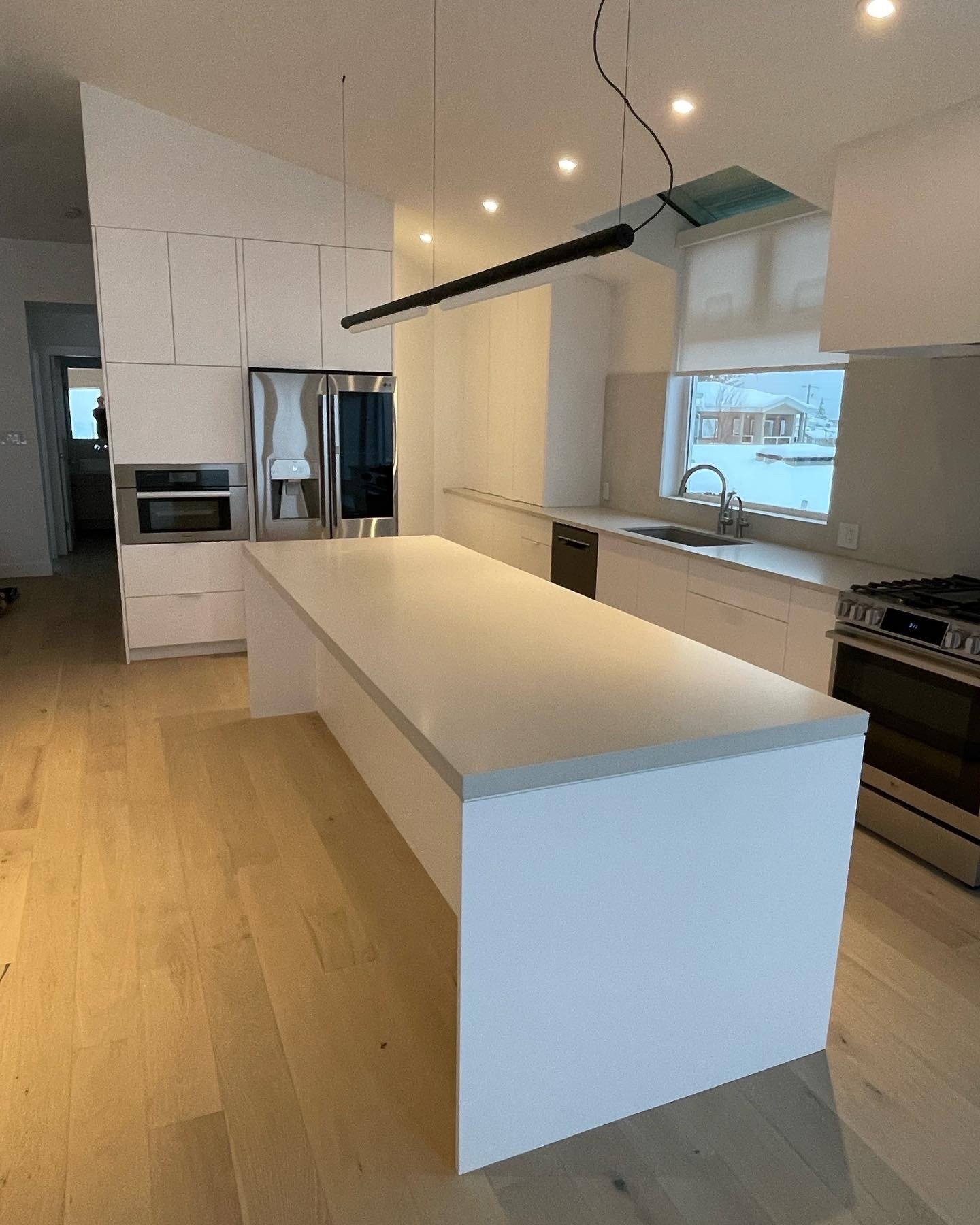 A bright modern kitchen space with a large white island, light wood floors, a stainless steel gas range, and a long black light.