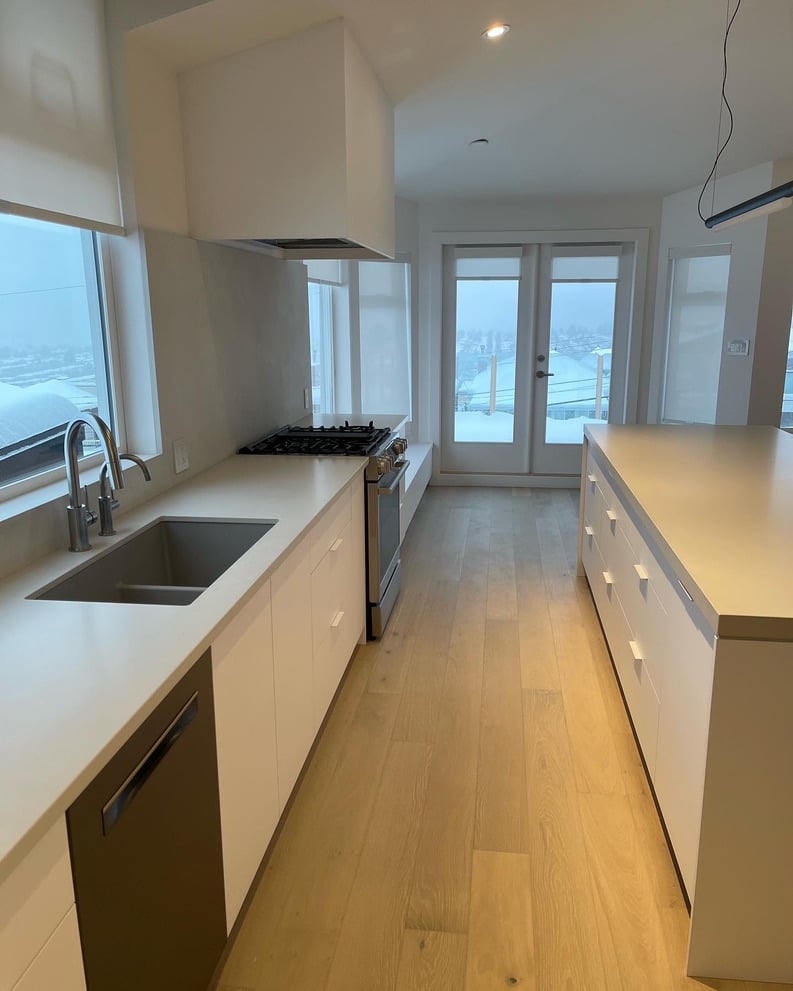 A long bright kitchen featuring a white island, white cabinets, a stainless steel gas range, and glass doors leading outside.