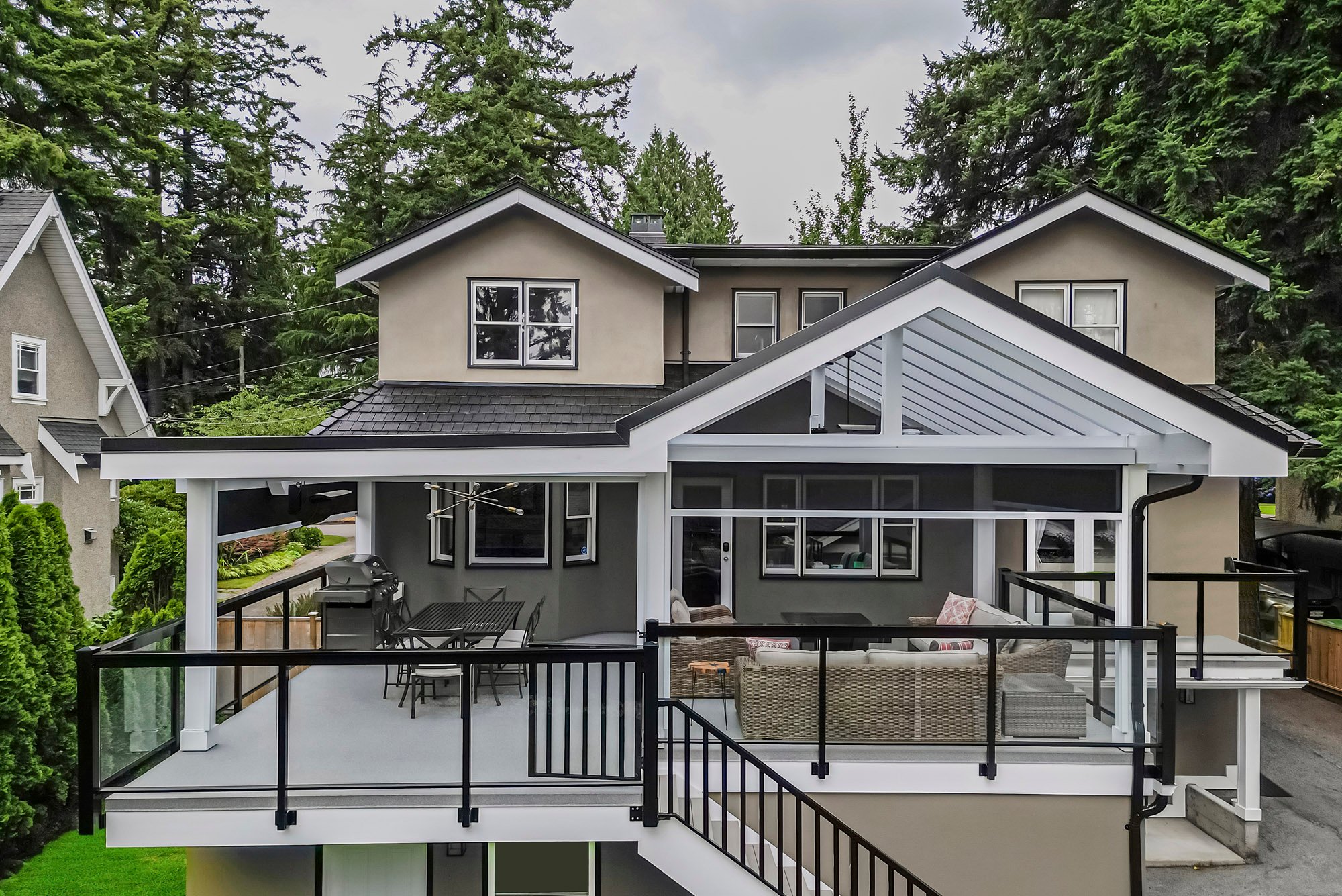 Elevated straight-on exterior view showing a large covered second-story deck with glass railings, outdoor seating, and a grill.