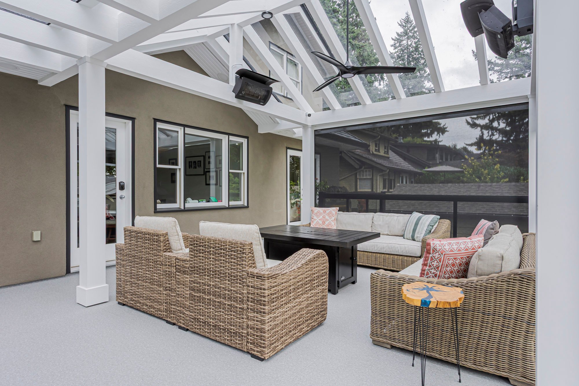 A comfortable outdoor lounge area on a covered deck, featuring large wicker sofas surrounding a black fire pit table.