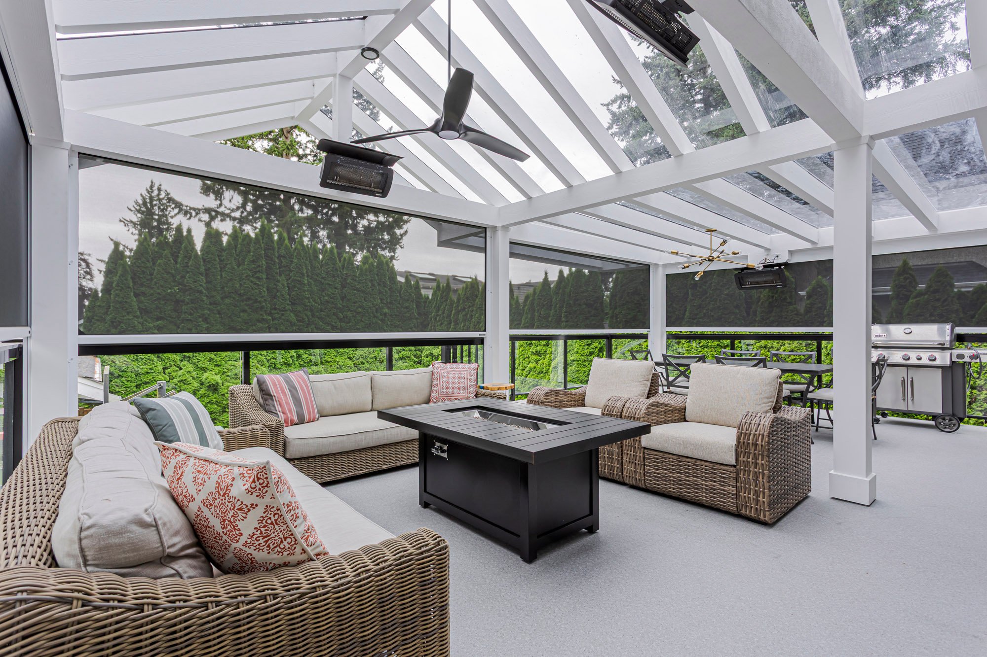 A spacious covered outdoor deck featuring a wicker lounge set, black fire pit, and an outdoor dining area with a gas grill.